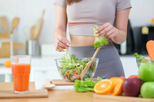 A woman skillfully prepares a colorful salad, combining fresh vegetables and fruits in a bright kitchen setting.