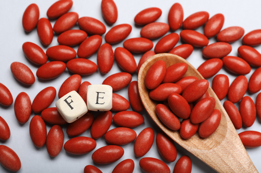 Red iron tablets with 'FB' lettering, shown beside a wooden spoon filled with tablets for a minimalistic and health-focused design.