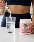 Person adding powder to a glass of water next to a container of 'life botanics' supplement.